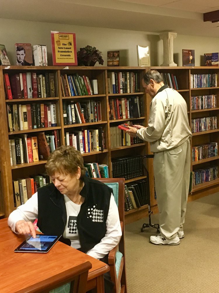 Two people in a library, one browsing books and the other using a tablet.