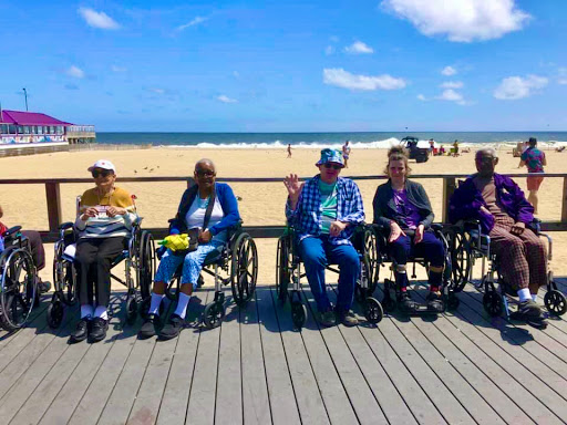A group of elderly individuals in wheelchairs enjoying a sunny day at the beach.