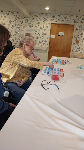 An engagement activity at a care facility, where an elderly woman sorts or arranges items on the table.