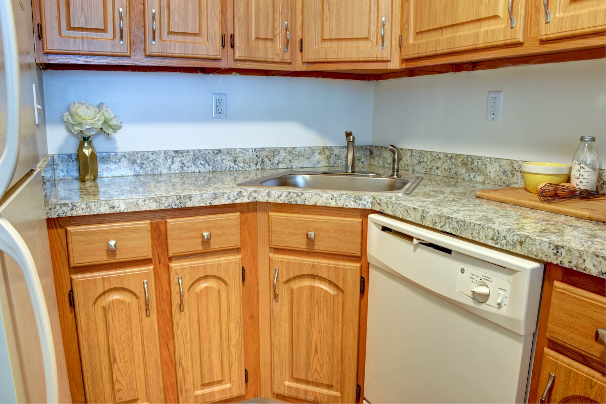 A kitchen with wooden cabinets and a granite countertop, featuring a sink and dishwasher.