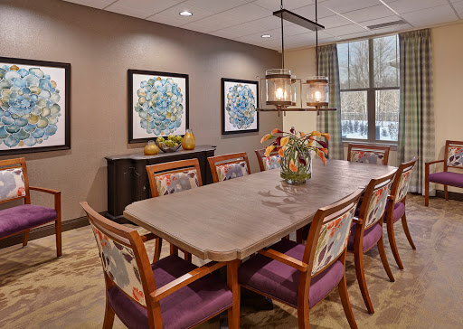 A modern dining room featuring a long wooden table, colorful chairs, and elegant lighting.