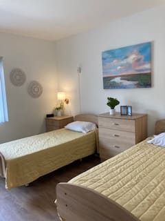 A cozy bedroom with two twin beds adorned with yellow bedspreads, featuring a dresser and a lamp, complemented by wall art and decor.