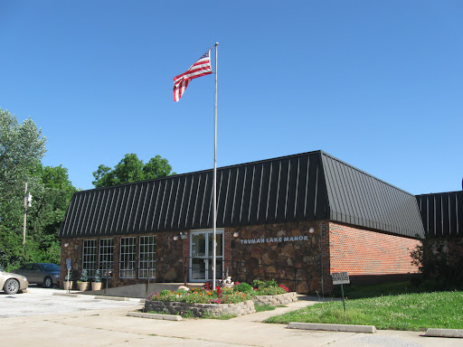 A brick building with a black roof and an American flag flying in front under a clear blue sky.