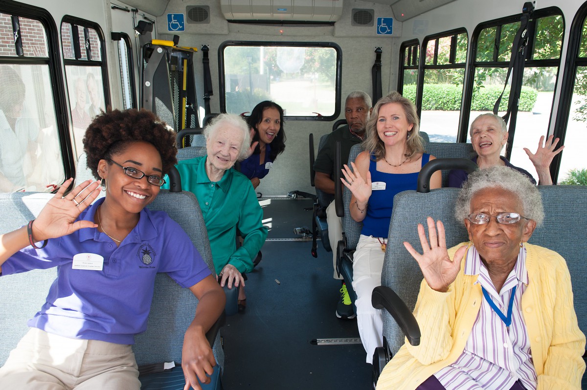 A group of people smiling and waving while sitting inside a bus.