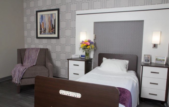 A cozy bedroom featuring a single bed, bedside table with flowers, and wall art.