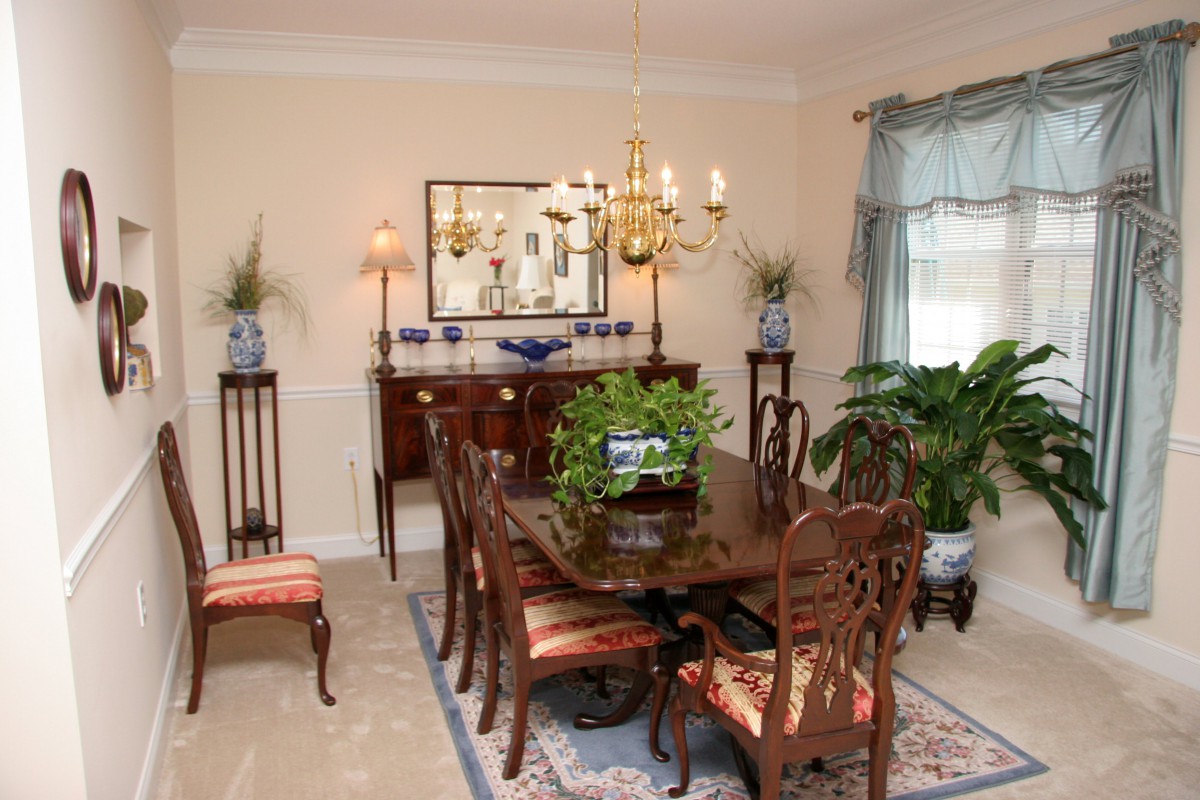 A traditional dining room with elegant furniture, a chandelier, and decorative elements such as plants and artwork.