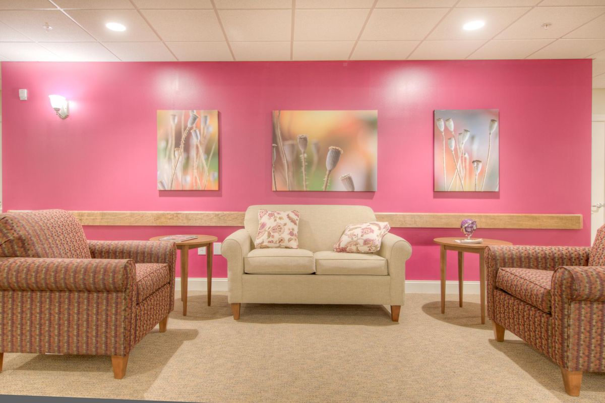 A cozy waiting room with a pink accent wall, featuring comfortable seating and artwork.