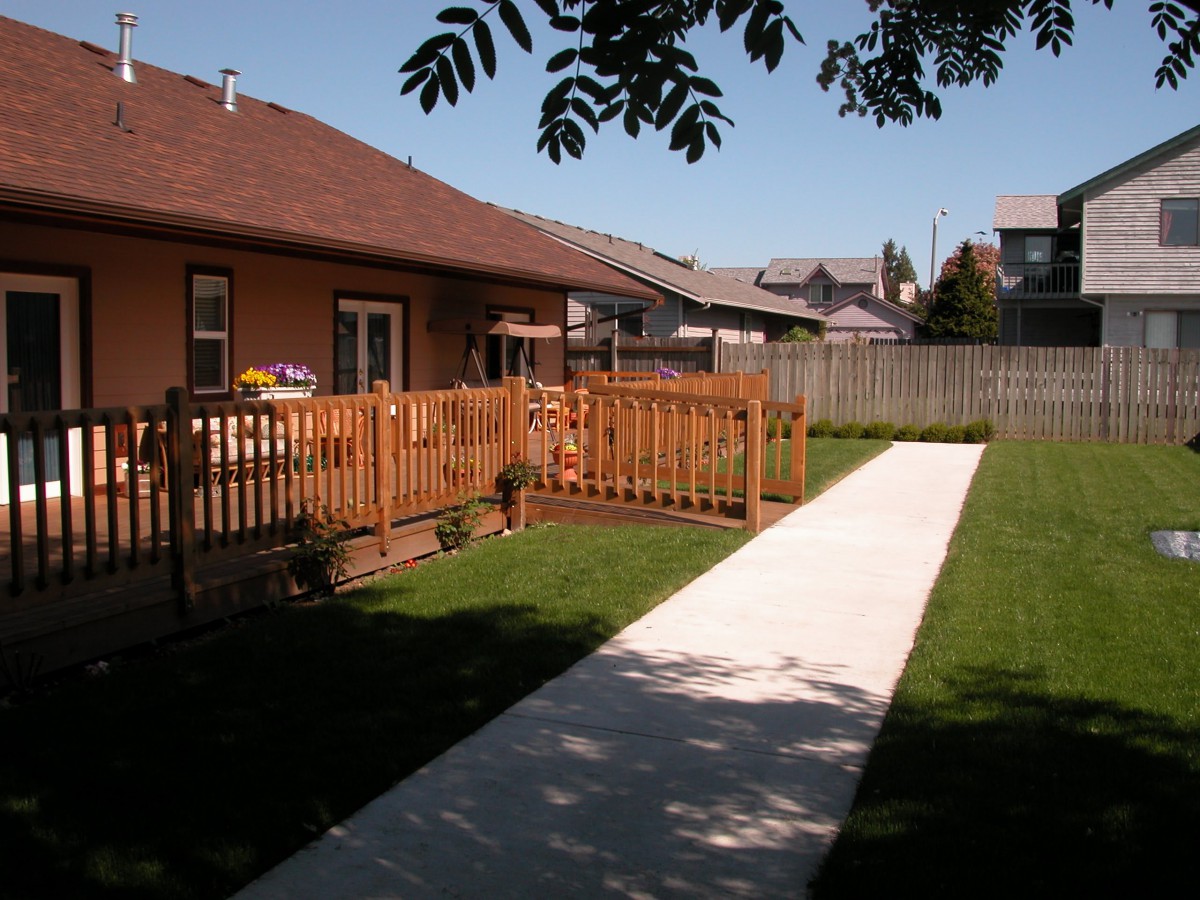 A backyard with a wooden fence and a concrete sidewalk leading to a house.