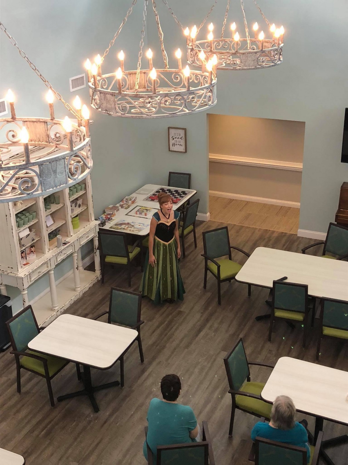 A dining area setup for an event with a person dressed in costume and elegant chandeliers overhead.
