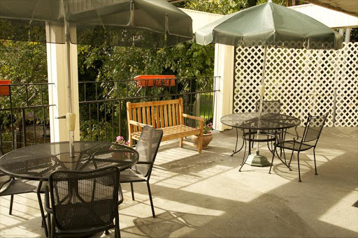 A cozy outdoor patio area featuring tables, chairs, and a wooden bench under sunshades.