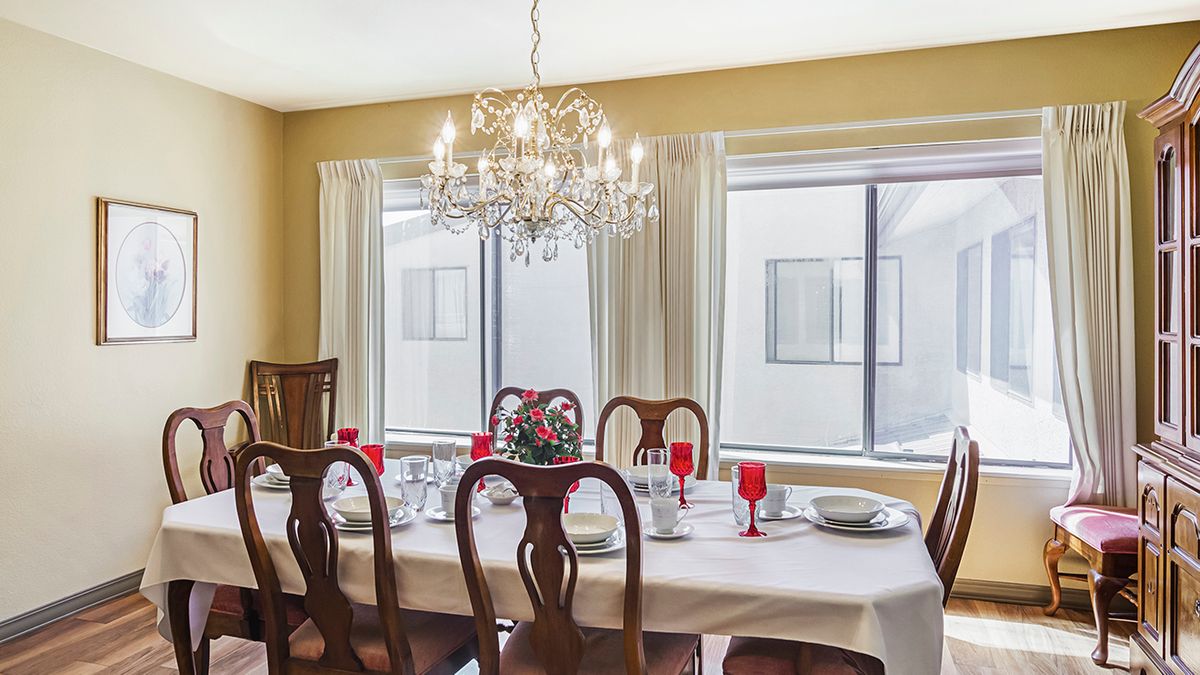 An elegantly set dining room table with a chandelier overhead and large windows providing natural light.