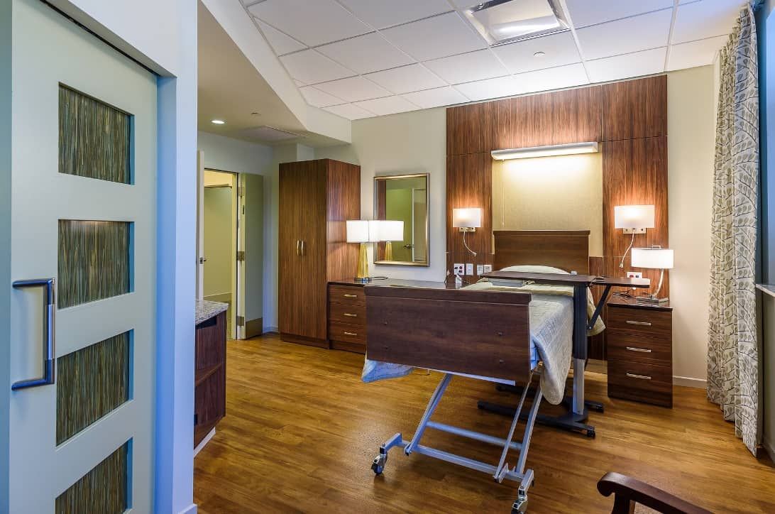 A well-furnished hospital room with a bed and wooden interior elements.