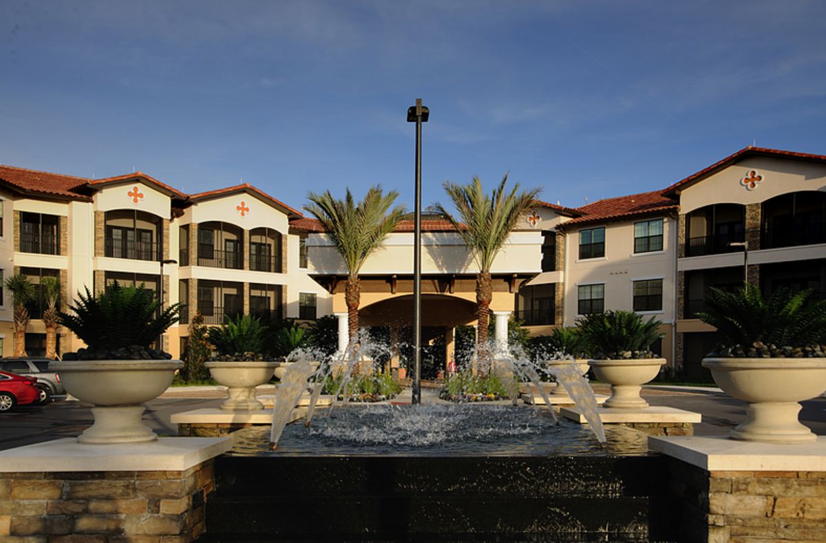 A beautiful courtyard featuring a central fountain surrounded by palm trees and a two-story building in the background.