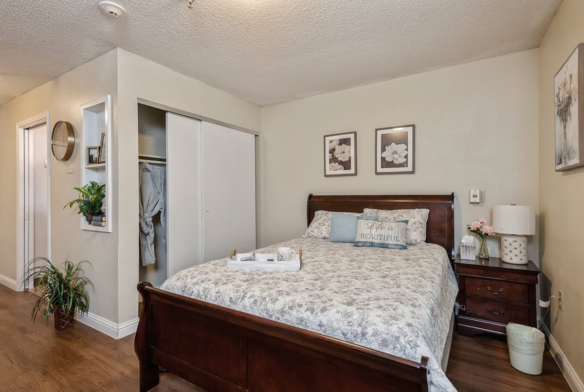 A cozy bedroom with a wooden bed, floral bedding, and a nightstand beside an open closet.