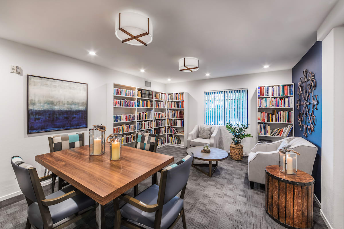 A cozy library room with bookshelves, a wooden table, and comfortable seating.