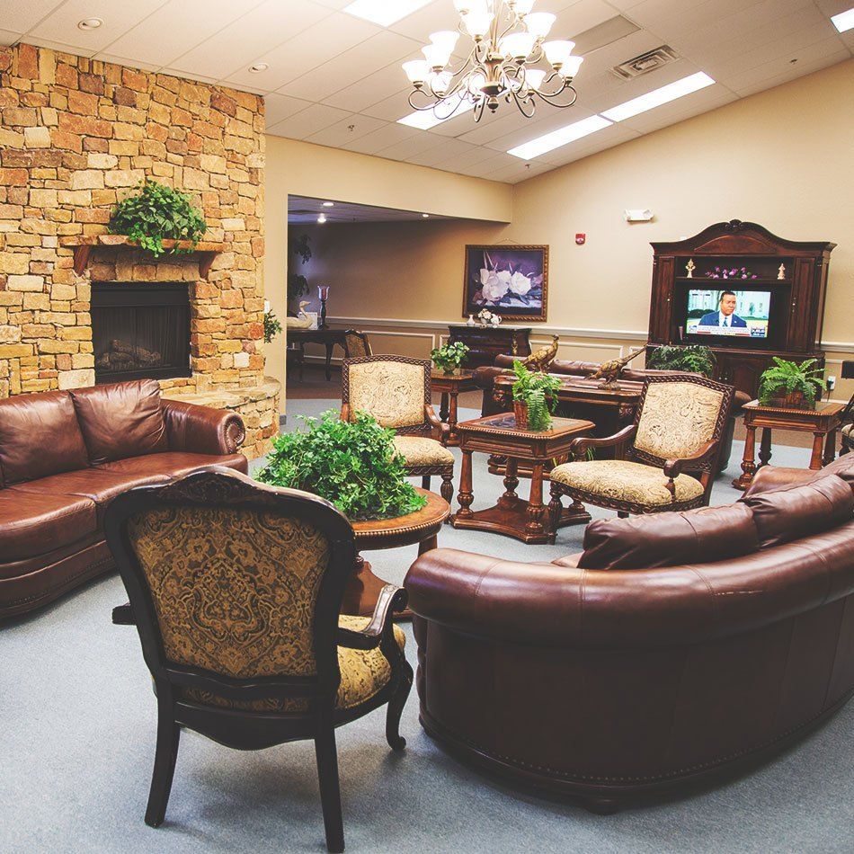 A cozy lounge area featuring leather sofas, armchairs, a fireplace, and indoor plants under a chandelier.