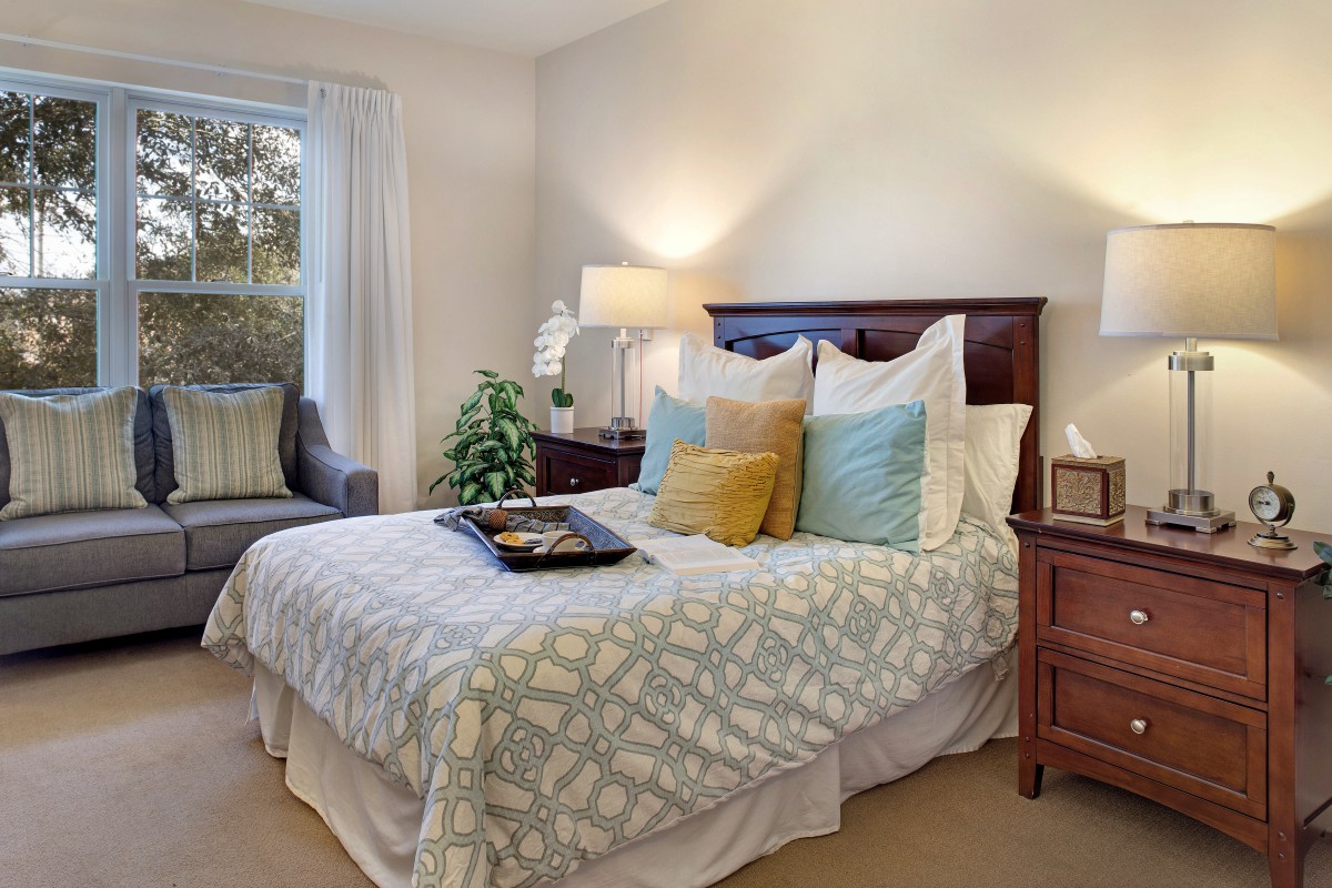 A cozy bedroom with a neatly made bed, soft pillows, and warm lighting.