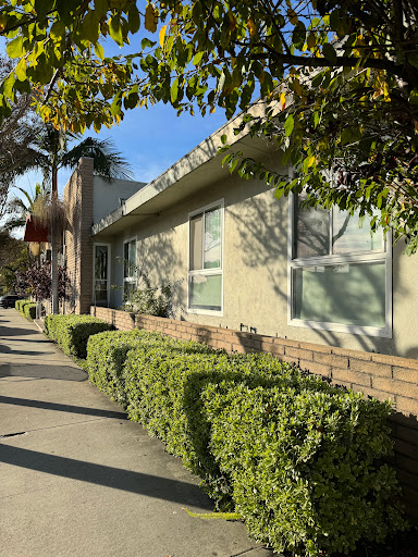A sunny day showcasing a well-maintained residential building with neatly trimmed bushes along the sidewalk.