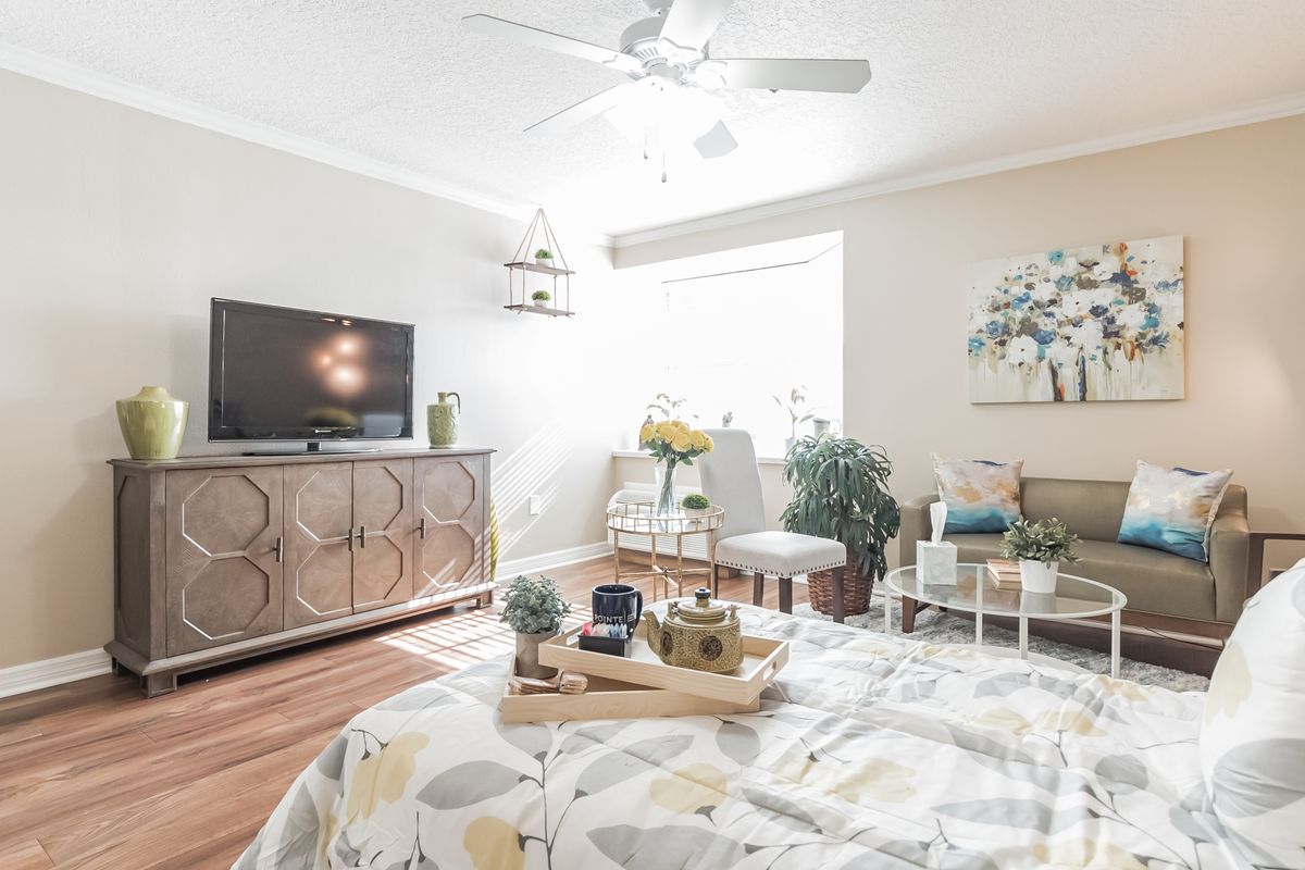 A modern and spacious bedroom with pastel colors, featuring a stylish TV stand, abundant natural light, and lush plants.