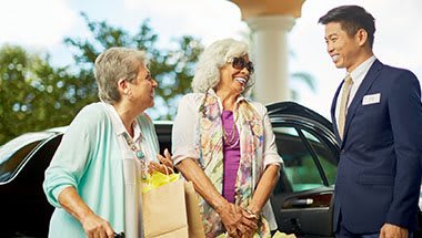 Two senior women enjoying a shopping trip, standing by a car and smiling.