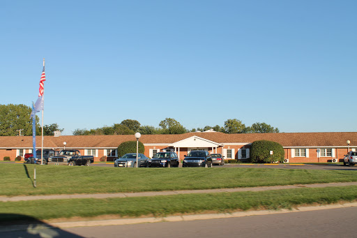 A view of a single-story residential building surrounded by vehicles and green grass under a clear blue sky.