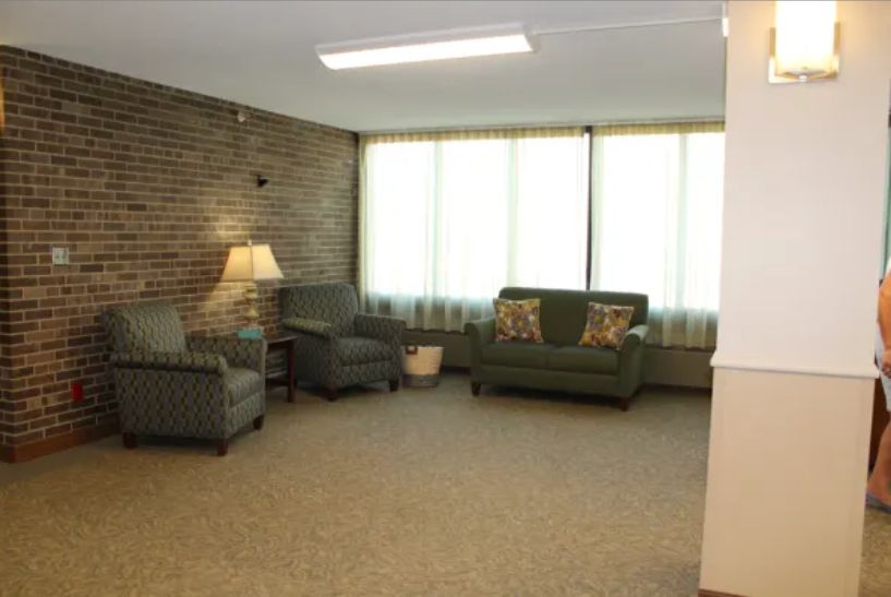 A cozy living room featuring a sofa, armchair, and lamp against a brick wall.