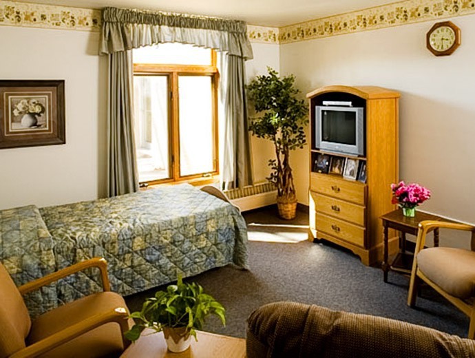 A cozy bedroom featuring a bed, wooden furniture, a television, and decorative plants.