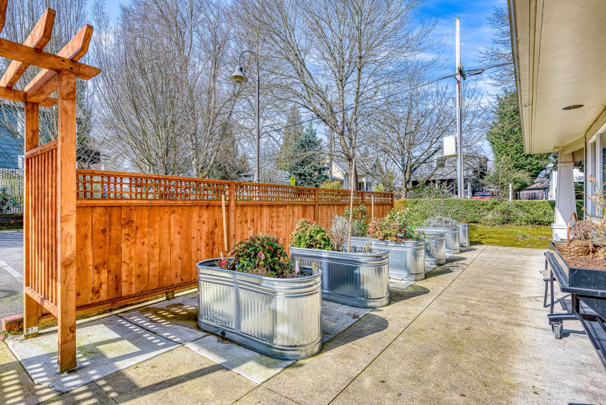A row of metal planters with greenery against a wooden fence on a sunny day.