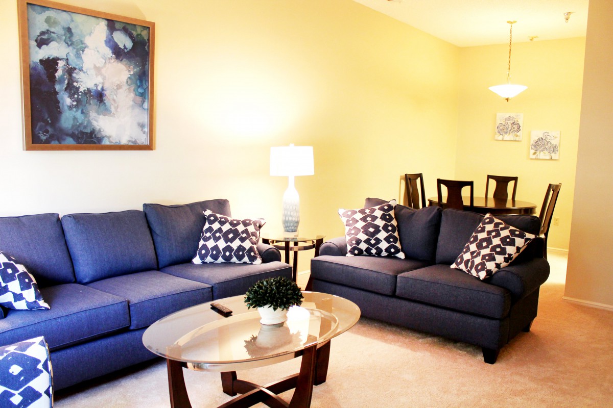 A cozy living room with blue sofas and a wooden coffee table, featuring stylish decor and artwork on the wall.