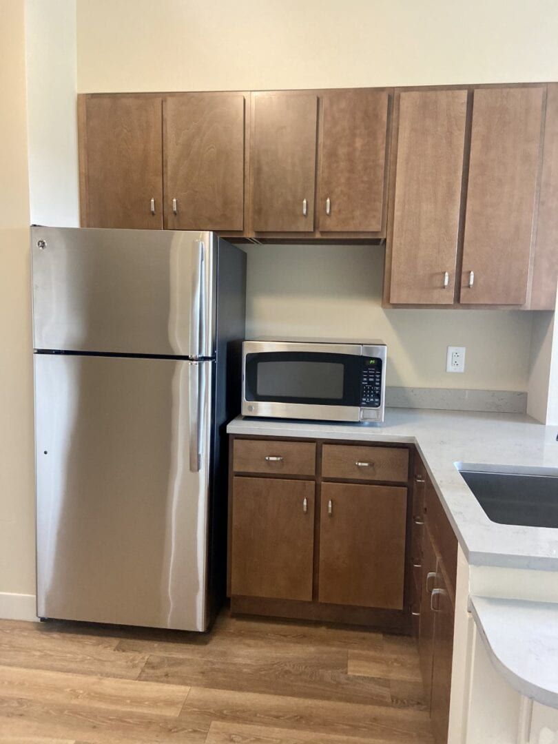 A modern kitchen corner with a stainless steel refrigerator, microwave, and wooden cabinets.