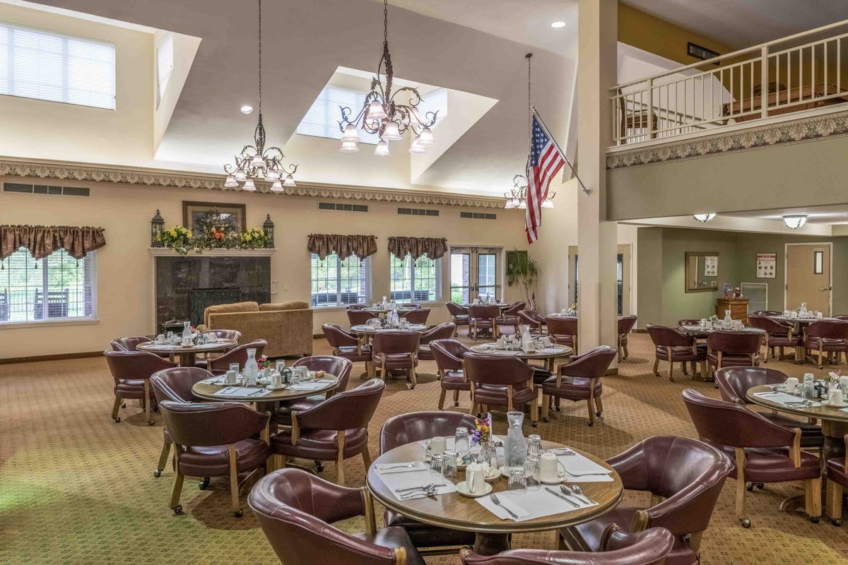 A dining room with neatly set tables and chairs, featuring chandeliers and an American flag.