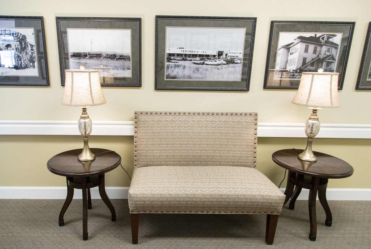 A cozy seating area with a sofa, side tables, and lamps against a backdrop of framed artwork.