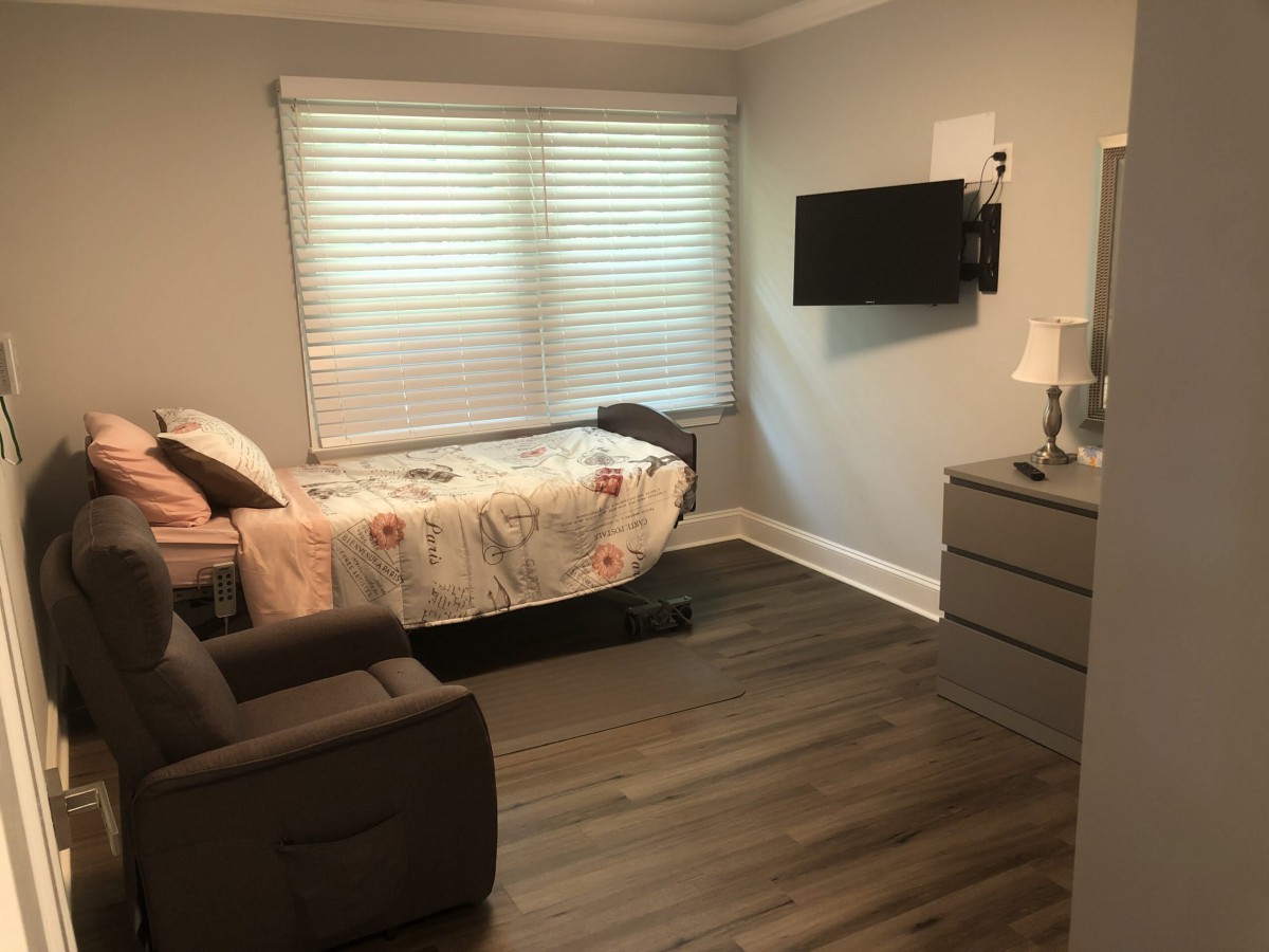 A cozy bedroom with a single bed, wall-mounted TV, and armchair.