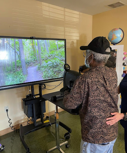 An elderly individual engages with a virtual reality nature experience, guided by a caregiver.
