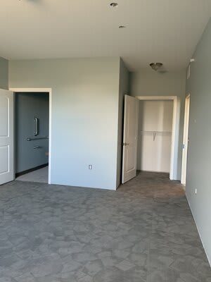 An empty room with carpeted flooring and open doors leading to adjacent areas.