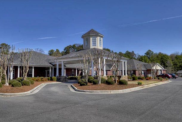 A building with a circular driveway, surrounded by trees and landscaping under a clear blue sky.