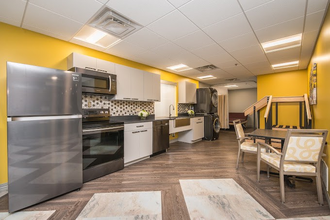 A modern kitchen with stainless steel appliances, yellow walls, and a seating area.