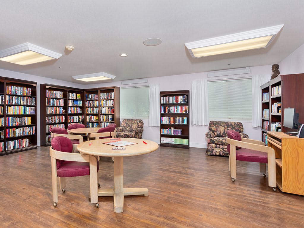 A cozy library reading area with round tables, chairs, and bookshelves lining the walls.
