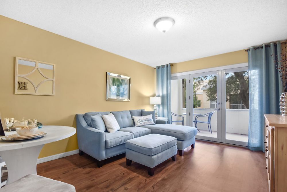 A modern living room with a blue sectional sofa and wooden flooring, featuring large sliding glass doors opening to a balcony.