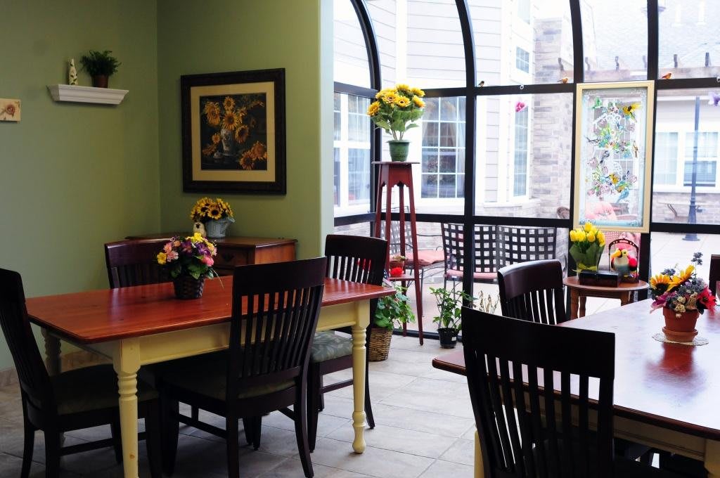 A cozy dining area with tables and chairs, adorned with floral arrangements, and a large window allowing natural light to fill the space.