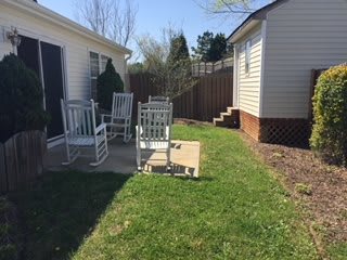 A sunny backyard patio with rocking chairs and a small grassy area.