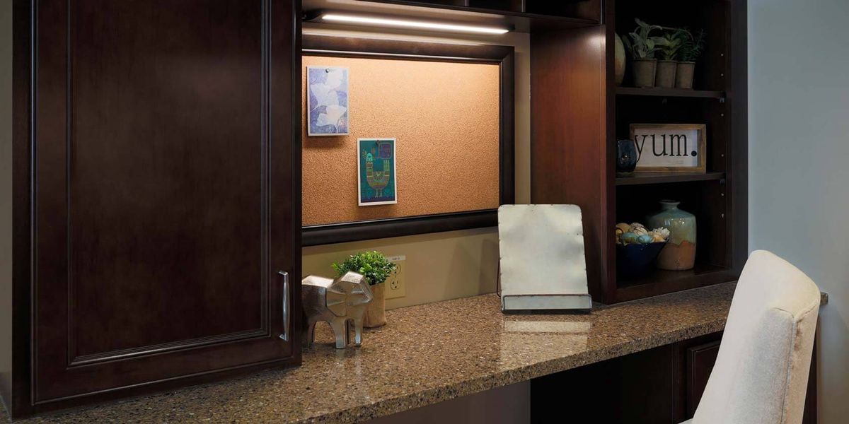 A cozy kitchen corner with a granite countertop, corkboard, and warm lighting.