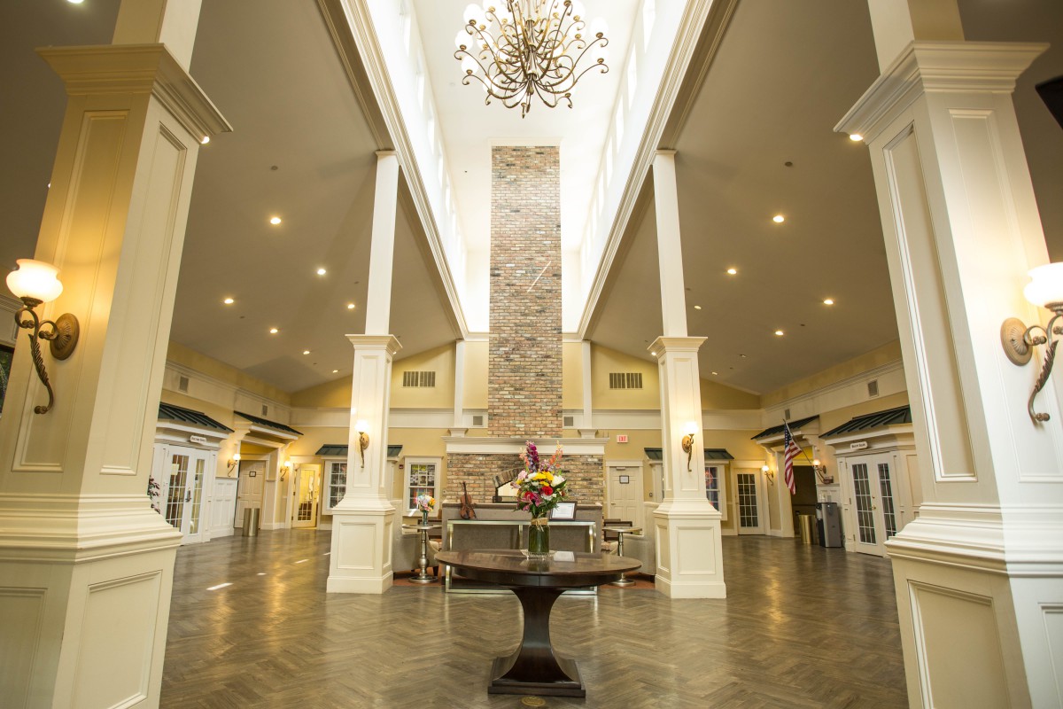 A spacious and elegantly designed lobby featuring a high ceiling with a central chandelier and symmetrical columns.