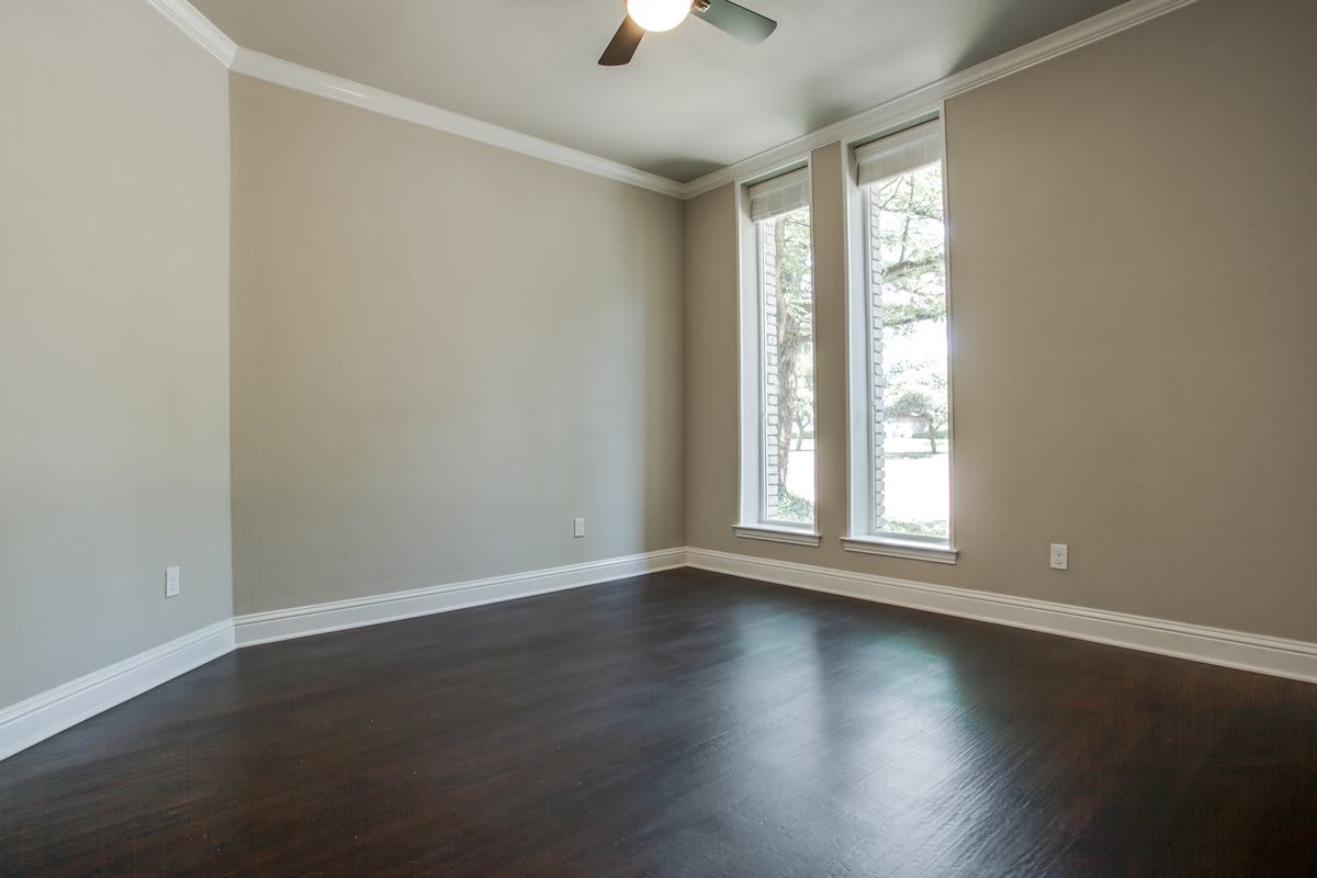 An empty room with hardwood flooring, large windows, and a ceiling fan.
