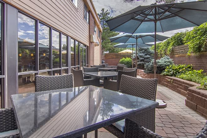 A cozy outdoor patio area with tables and chairs, shaded by large umbrellas, surrounded by greenery.