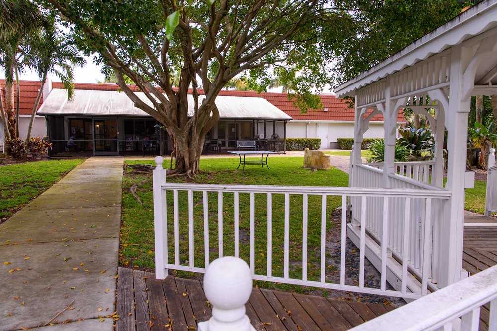 A tranquil garden view with a gazebo, lush greenery, and a white fence.