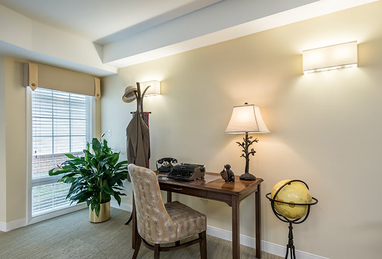 A cozy home office setup with a wooden desk, upholstered chair, and decorative items like a lamp and globe.