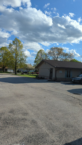 A peaceful residential scene with a house, trees, and a parking area under a partly cloudy sky.