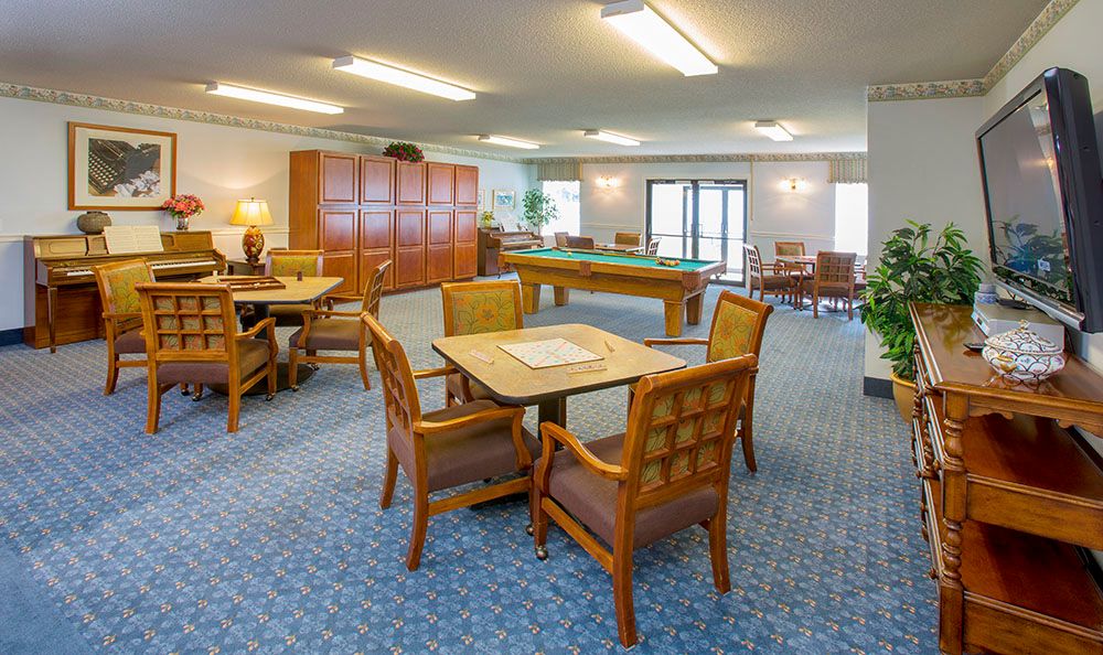 A spacious community room featuring a seating area with tables and chairs, and a billiards table.