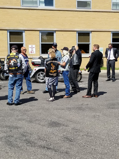 A diverse group of individuals, including bikers and formally dressed people, gathered outside near motorcycles.